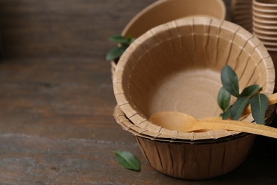 Photo of Set of disposable tableware and green leaves on wooden table, closeup. Space for text