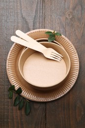 Photo of Set of disposable tableware and green leaves on wooden table, top view
