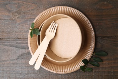 Photo of Set of disposable tableware and green leaves on wooden table, top view