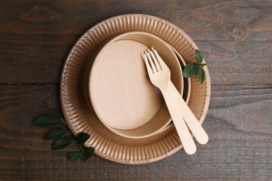Photo of Set of disposable tableware and green leaves on wooden table, top view