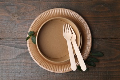 Photo of Set of disposable tableware and green leaves on wooden table, top view