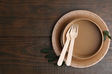 Photo of Set of disposable tableware and green leaves on wooden table, top view. Space for text