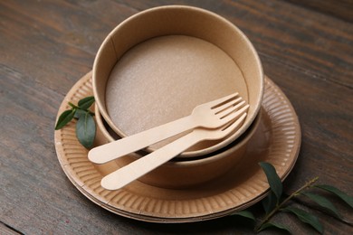 Photo of Set of disposable tableware and green leaves on wooden table, closeup