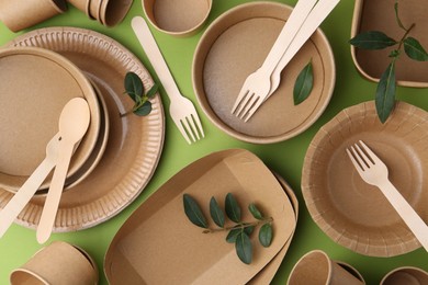 Photo of Set of disposable tableware and leaves on green background, flat lay