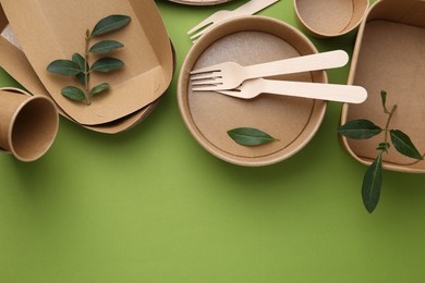 Photo of Set of disposable tableware and leaves on green background, flat lay. Space for text