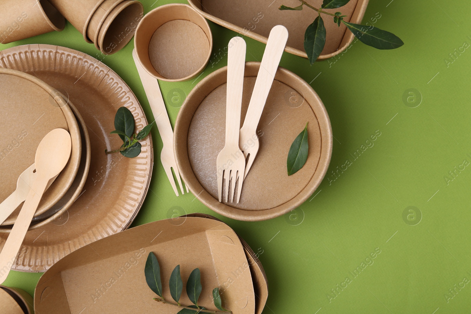 Photo of Set of disposable tableware and leaves on green background, flat lay. Space for text
