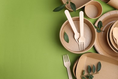 Photo of Set of disposable tableware and leaves on green background, flat lay. Space for text