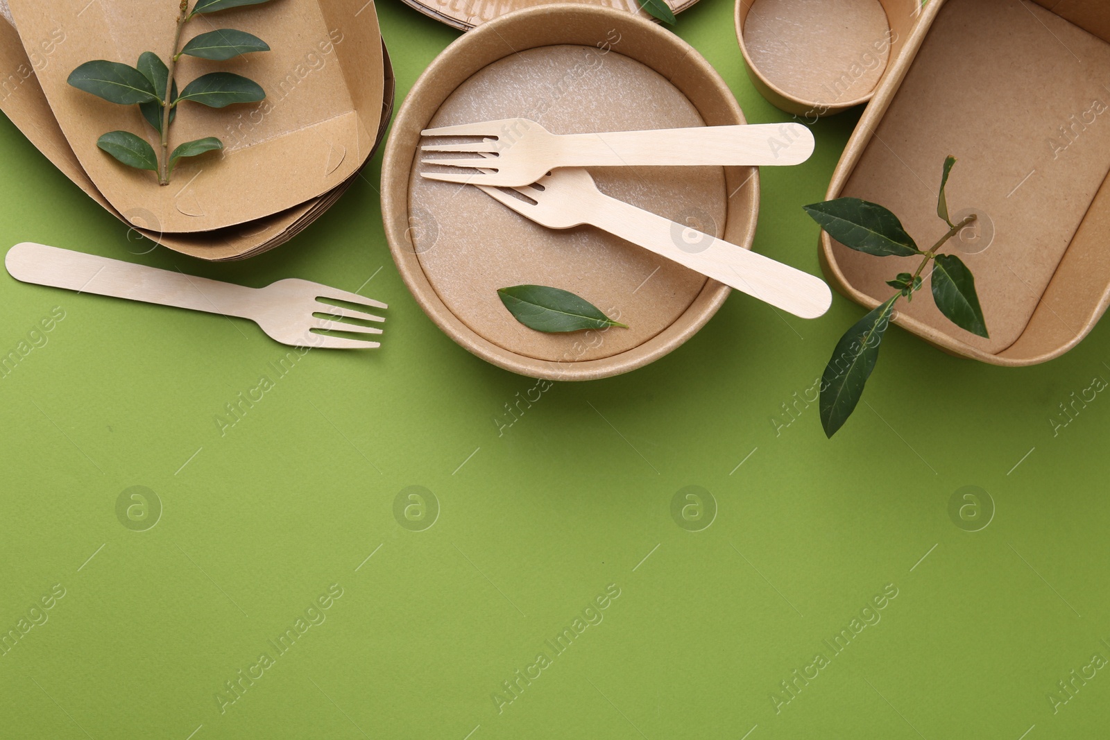 Photo of Set of disposable tableware and leaves on green background, flat lay. Space for text