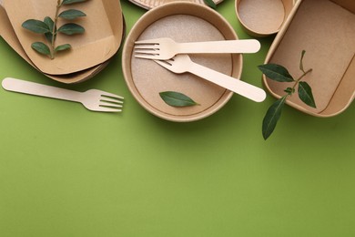 Photo of Set of disposable tableware and leaves on green background, flat lay. Space for text