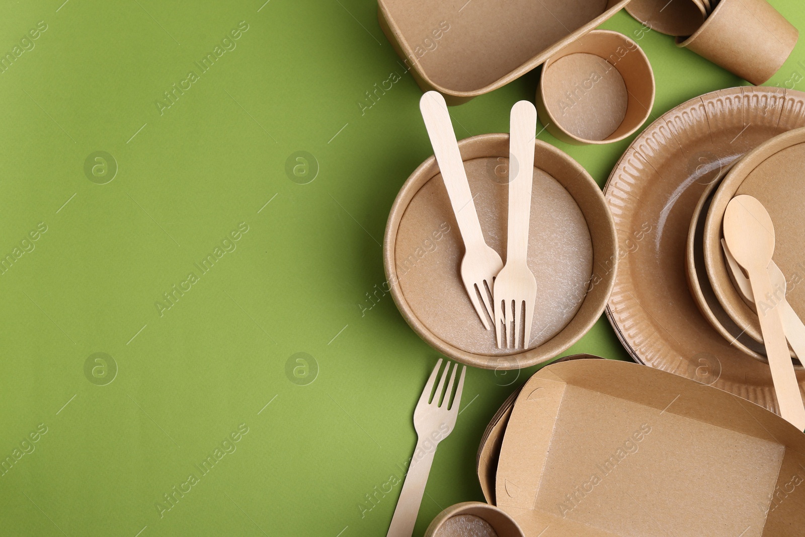 Photo of Set of disposable tableware on green background, flat lay. Space for text