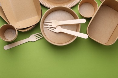 Photo of Set of disposable tableware on green background, flat lay. Space for text