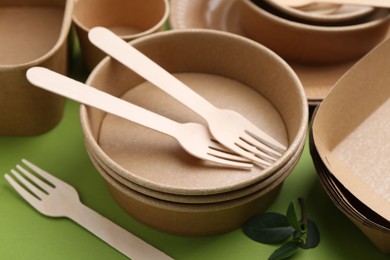 Photo of Set of disposable tableware and leaves on green background, closeup