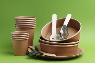 Photo of Set of disposable tableware and leaves on green background, closeup