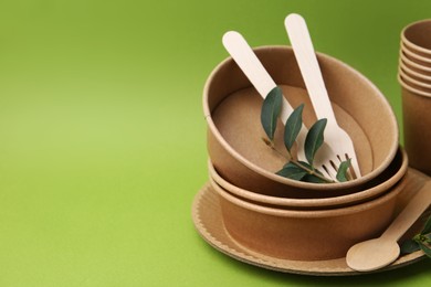 Photo of Set of disposable tableware and leaves on green background, closeup. Space for text