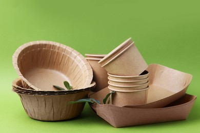 Photo of Set of disposable tableware and leaves on green background, closeup