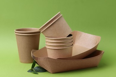 Photo of Set of disposable tableware and leaves on green background, closeup