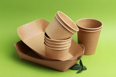 Photo of Set of disposable tableware and leaves on green background, closeup