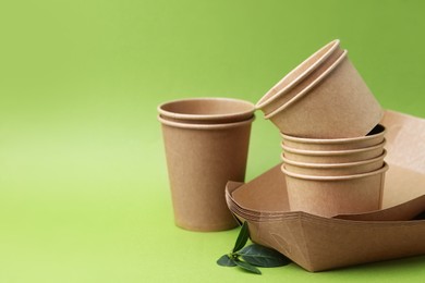 Photo of Set of disposable tableware and leaves on green background, closeup. Space for text
