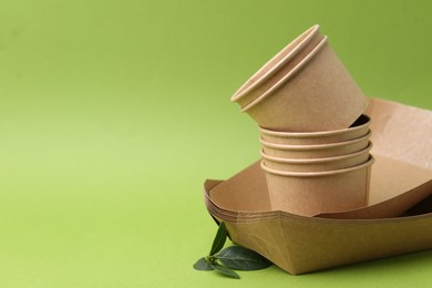 Photo of Set of disposable tableware and leaves on green background, closeup. Space for text