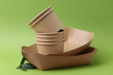 Photo of Set of disposable tableware and leaves on green background, closeup