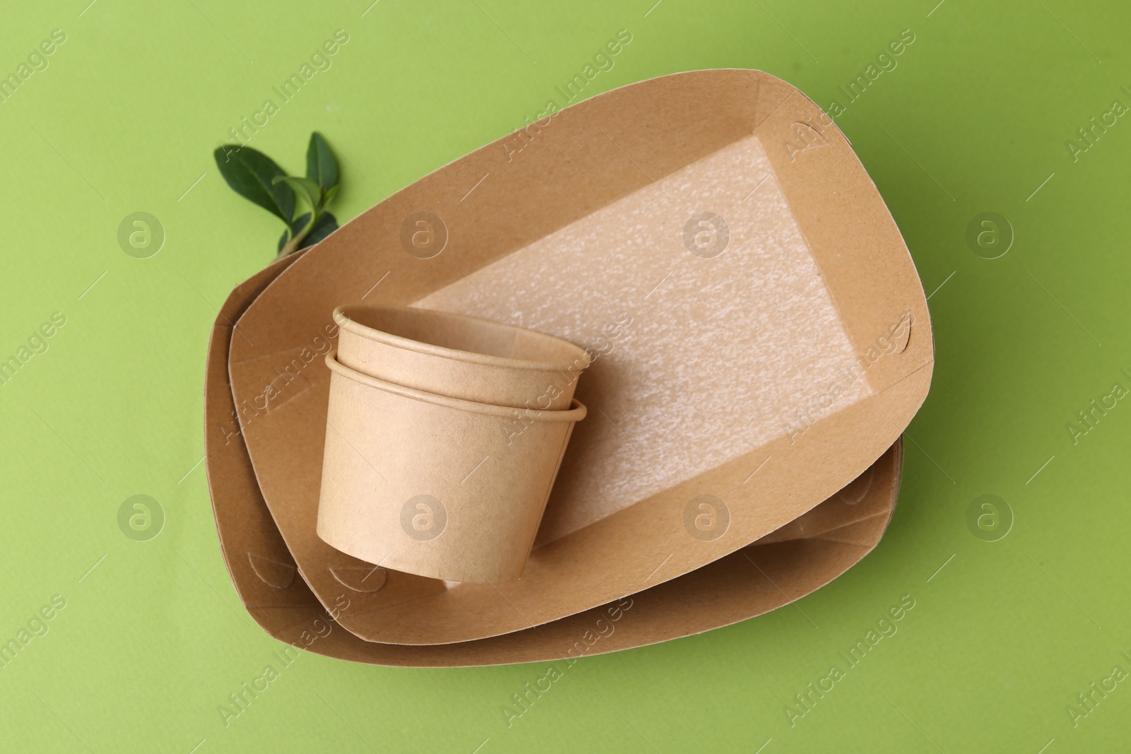 Photo of Set of disposable tableware and leaves on green background, top view