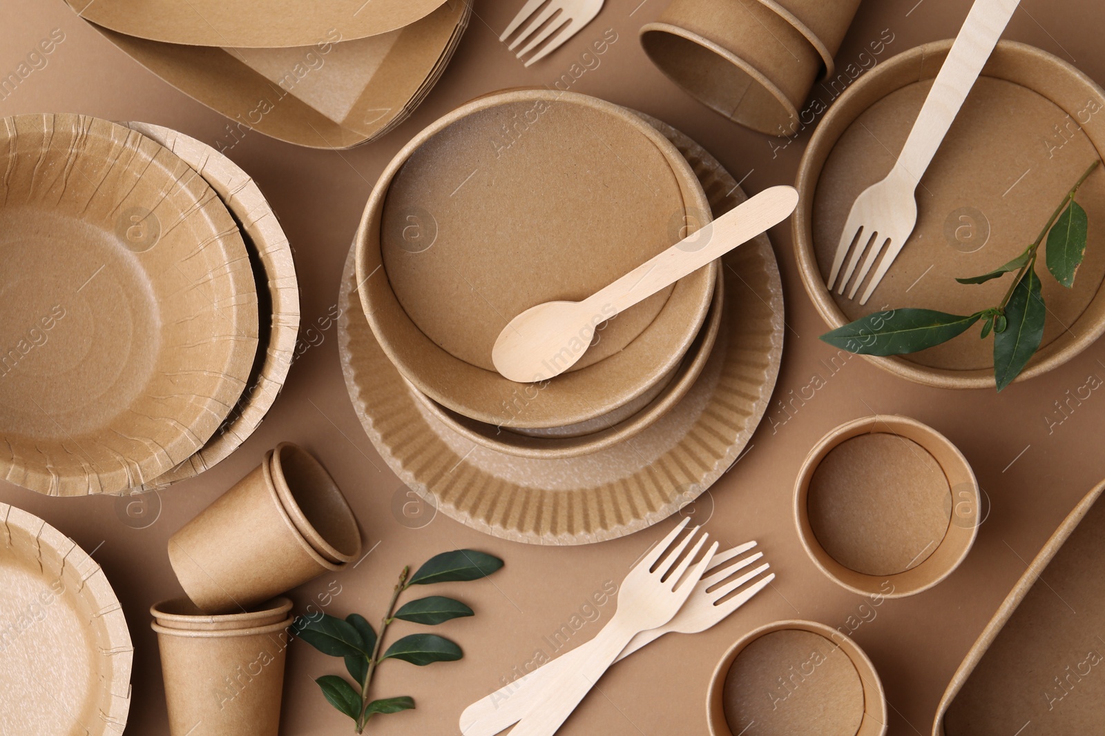 Set of disposable tableware and green leaves on brown background, flat lay Photo of Set of disposable tableware and green leaves on brown background, flat lay