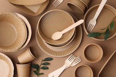 Photo of Set of disposable tableware and green leaves on brown background, flat lay