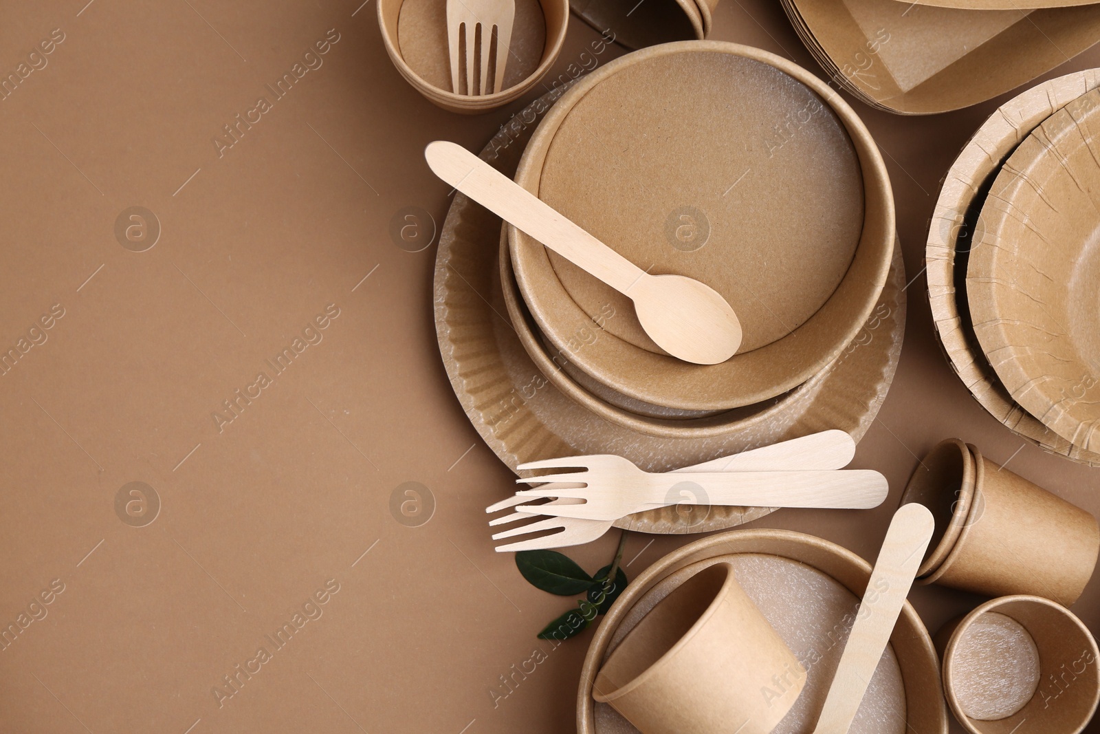 Set of disposable tableware and green leaves on brown background, flat lay. Space for text Photo of Set of disposable tableware and green leaves on brown background, flat lay. Space for text
