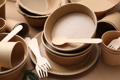 Photo of Set of disposable tableware and green leaves on brown background, closeup