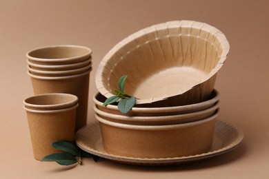 Photo of Set of disposable tableware and green leaves on brown background, closeup