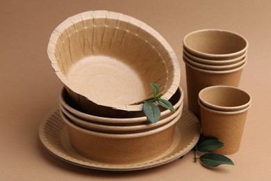 Photo of Set of disposable tableware and green leaves on brown background, closeup