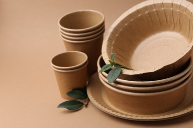 Photo of Set of disposable tableware and green leaves on brown background, closeup. Space for text