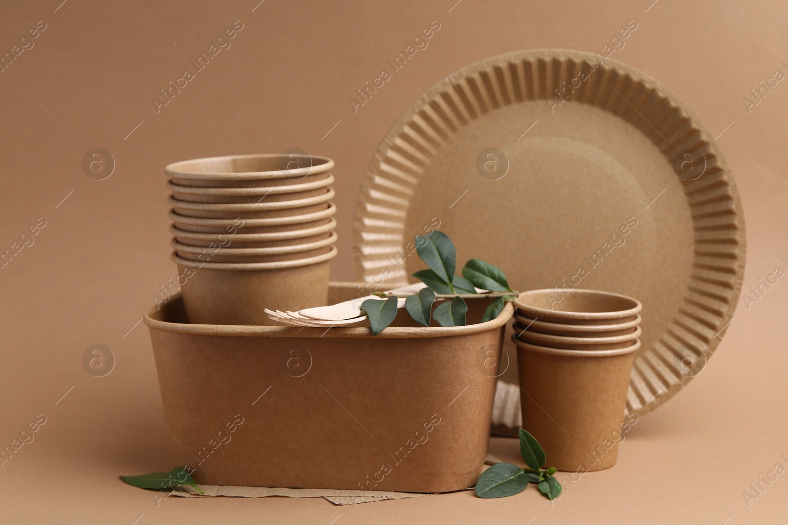 Set of disposable tableware and green leaves on brown background Photo of Set of disposable tableware and green leaves on brown background