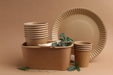 Photo of Set of disposable tableware and green leaves on brown background