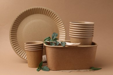 Photo of Set of disposable tableware and green leaves on brown background