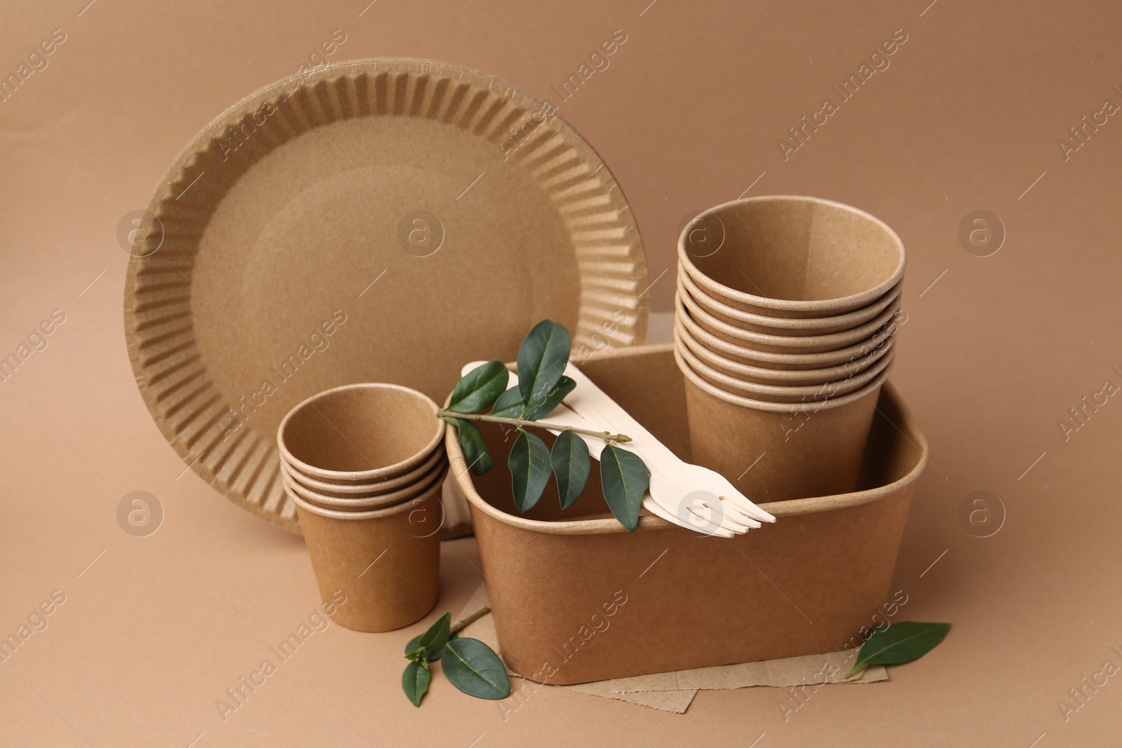 Set of disposable tableware and green leaves on brown background Photo of Set of disposable tableware and green leaves on brown background