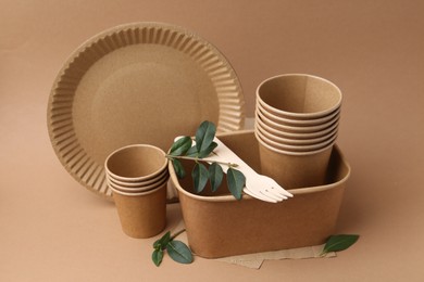 Photo of Set of disposable tableware and green leaves on brown background