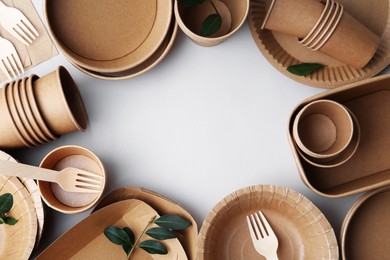 Photo of Set of disposable tableware and green leaves on white background, flat lay. Space for text