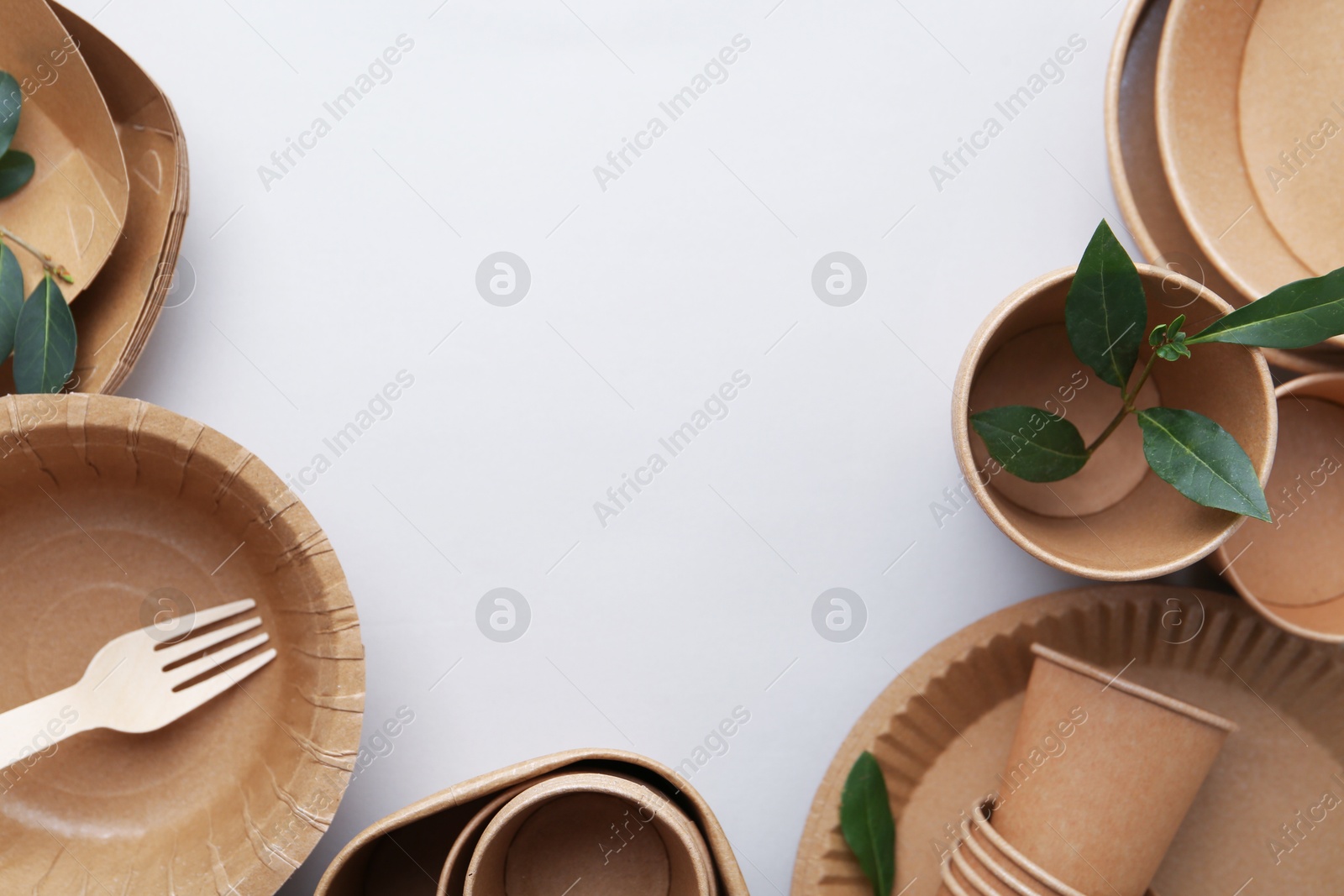 Set of disposable tableware and green leaves on white background, flat lay. Space for text Photo of Set of disposable tableware and green leaves on white background, flat lay. Space for text
