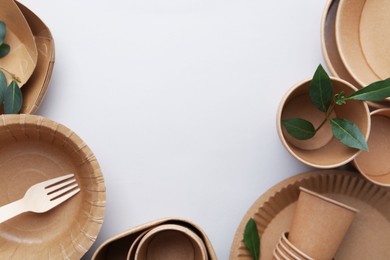 Photo of Set of disposable tableware and green leaves on white background, flat lay. Space for text