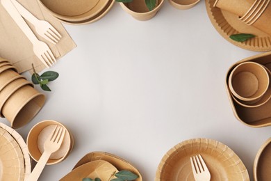 Photo of Set of disposable tableware and green leaves on white background, flat lay. Space for text