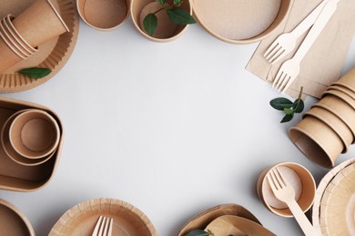 Photo of Set of disposable tableware and green leaves on white background, flat lay. Space for text