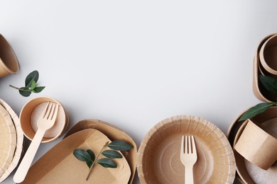 Photo of Set of disposable tableware and green leaves on white background, flat lay. Space for text