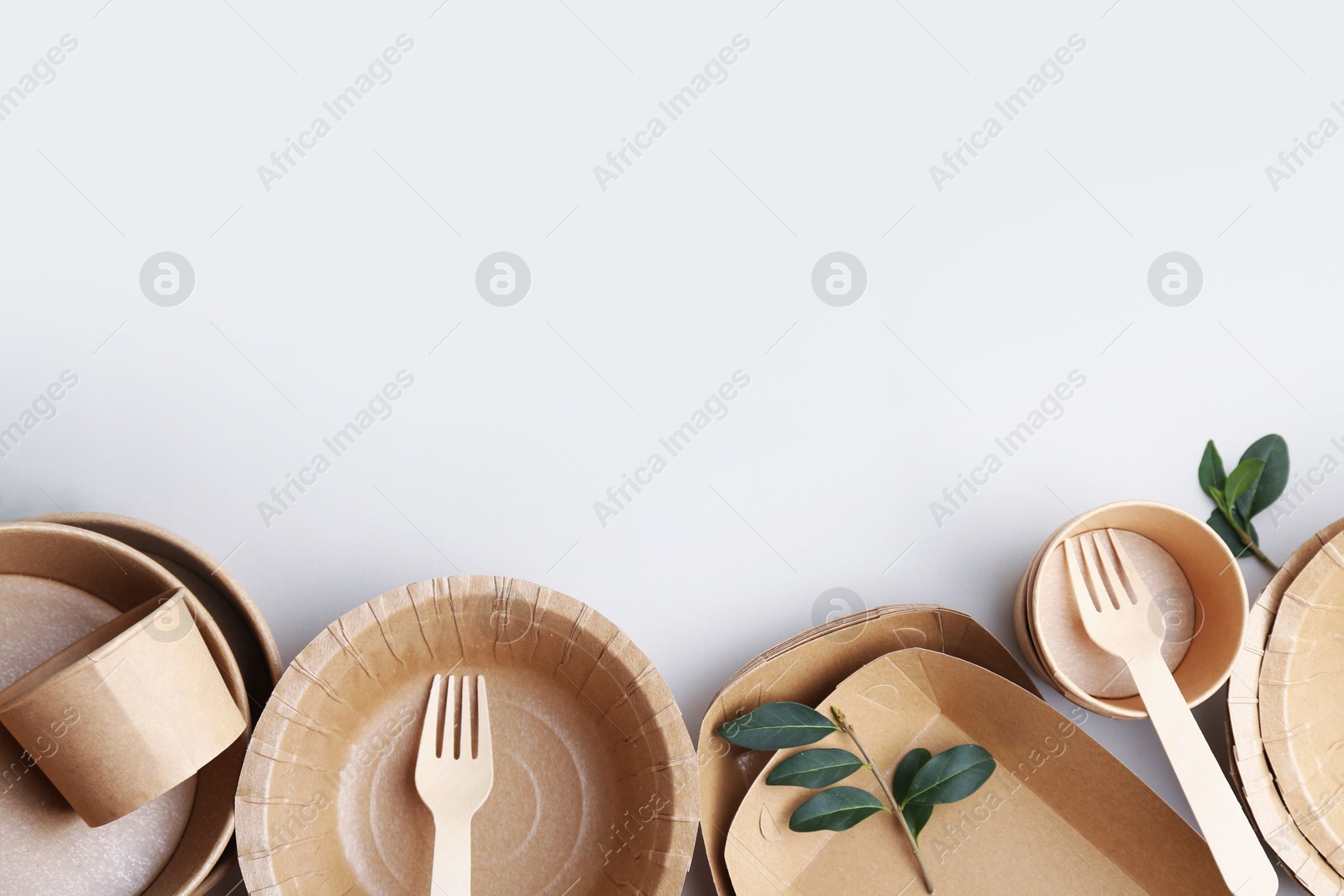 Set of disposable tableware and green leaves on white background, flat lay. Space for text Photo of Set of disposable tableware and green leaves on white background, flat lay. Space for text
