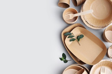 Photo of Set of disposable tableware and green leaves on white background, flat lay. Space for text