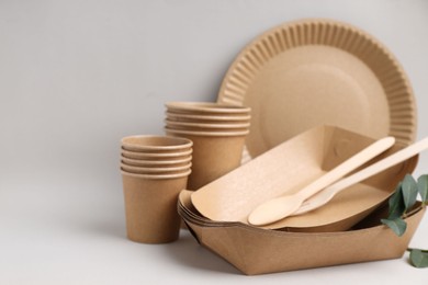 Photo of Set of disposable tableware and green leaves on light grey background, closeup. Space for text