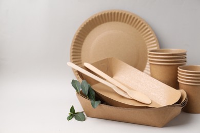 Photo of Set of disposable tableware and green leaves on light grey background, closeup. Space for text