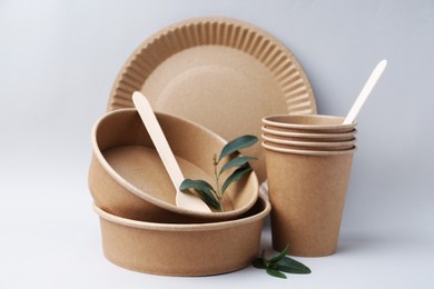 Photo of Set of disposable tableware and green leaves on light grey background, closeup