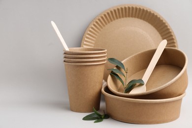 Photo of Set of disposable tableware and green leaves on light grey background, closeup. Space for text