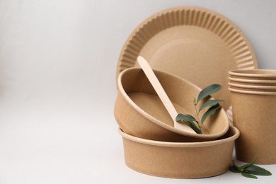 Photo of Set of disposable tableware and green leaves on light grey background, closeup. Space for text